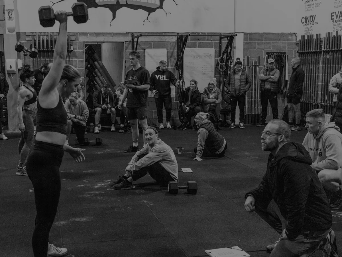 A coached CrossFit class mid-workout, dumbbells overhead